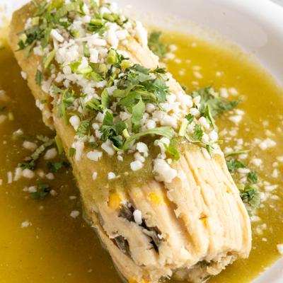 Tamale covered in green sauce cheese and cilantro.
