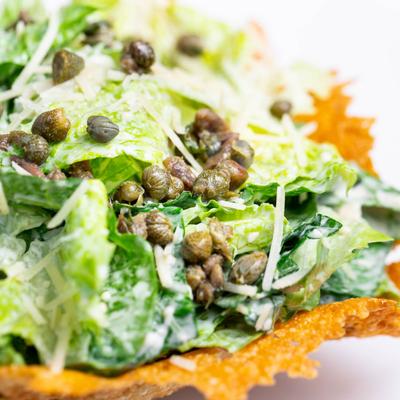 Caesar Salad, with romaine lettuce, dressing, parmesan crisps, capers, and cheese