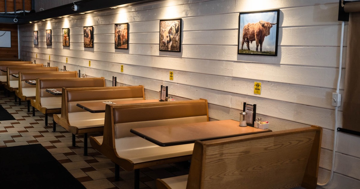 Interior seating area with rows of wooden booths and cattle pictures on the white wall