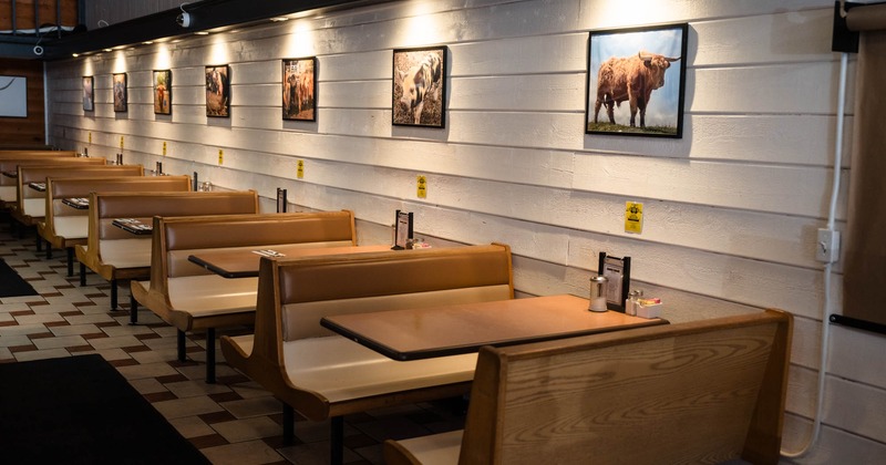 Interior seating area with rows of wooden booths and cattle pictures on the white wall