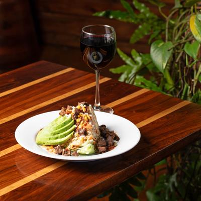 Wedge salad with avocado and steak, served with red wine.