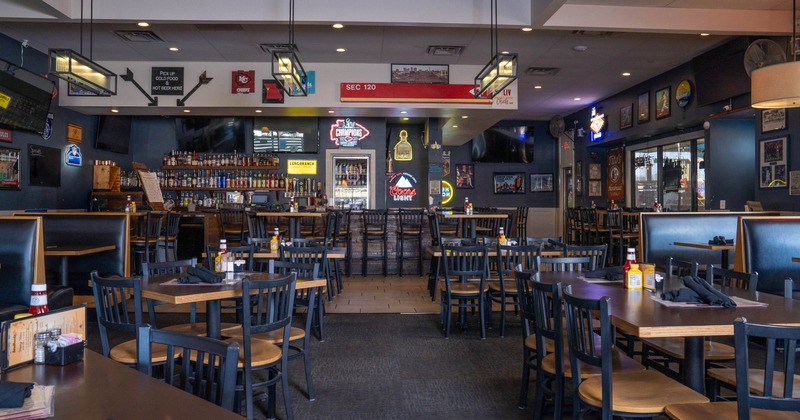 Sports-themed interior decorated with sports memorabilia and neon signs; wooden tables and chairs