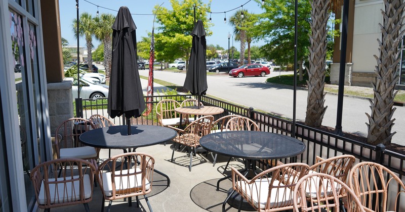 Outdoor dining area with round tables, wicker chairs, and black umbrellas