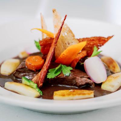 Dish with meat, carrot ribbons, bacon, roasted potatoes, radishes and parsley, close up.