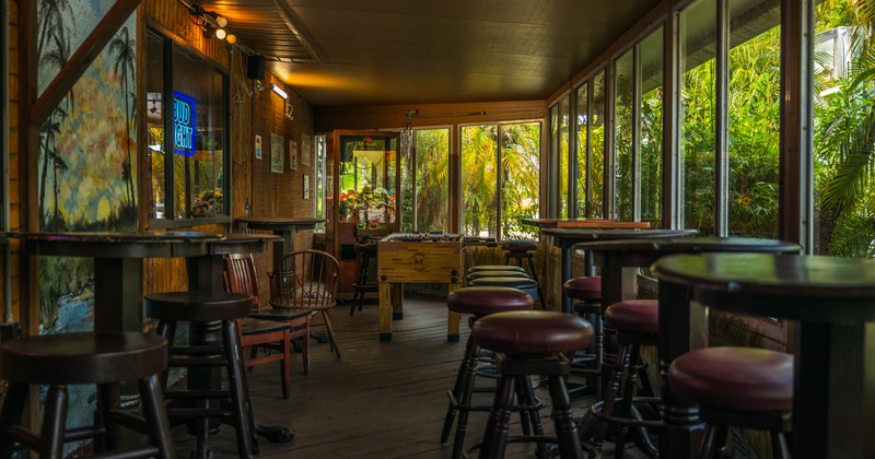 Interior of a cozy bar featuring wooden paneling, tall round tables, and bar stools
