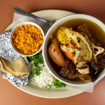 Caldo de res served with sides of red rice, tortillas, and fresh onion and cilantro.