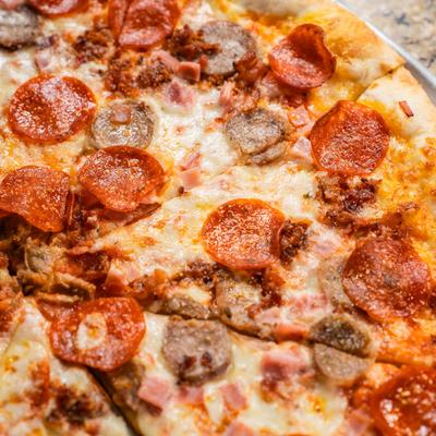A close-up of a pizza topped with pepperoni, sausage, bacon, and ham.