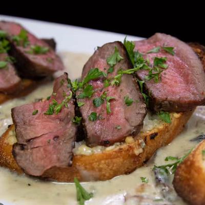 Slices of medium-rare beef on toasted bread with creamy sauce, garnished with parsley.