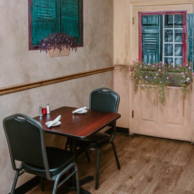 A  set two-top table with a mural of green shutters and a window box of flowers.