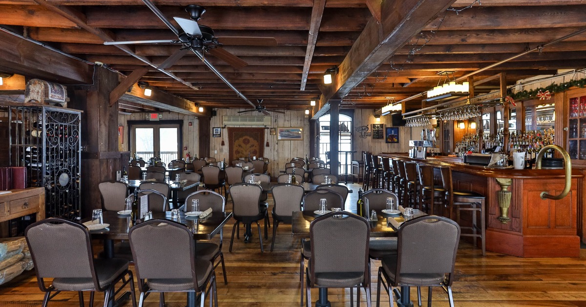 Interior rustic dining area with wooden tables, chairs, and a bar on the right side