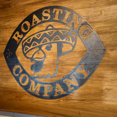 The Roasting Company logo on a wooden wall.