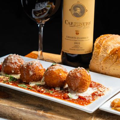 Arancini served with marinara sauce, alongside bottle and glass of red wine.