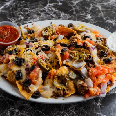 Nachos topped with cheese, taco meat, tomatoes, black olives, onions, and jalapenos.