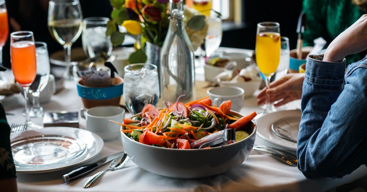 Guests enjoying drinks at a round table with place setting and a served salad, close up