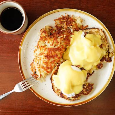 Eggs Benedict topped with hollandaise sauce, served with hash browns and a coffee.