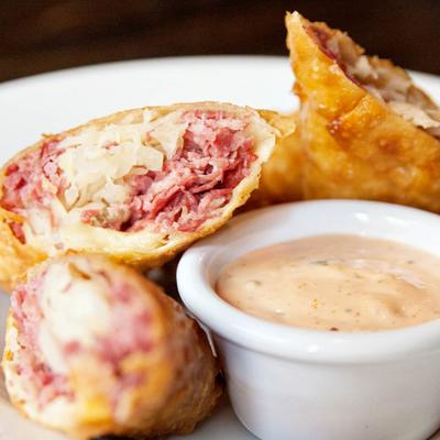Reuben egg rolls served with a sauce for dipping.