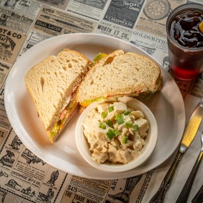 Sandwich and a side dish of potato salad serrved on a plate.