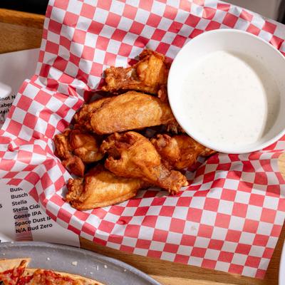 Chicken wings served with ranch dressing on red-and-white checkered paper.