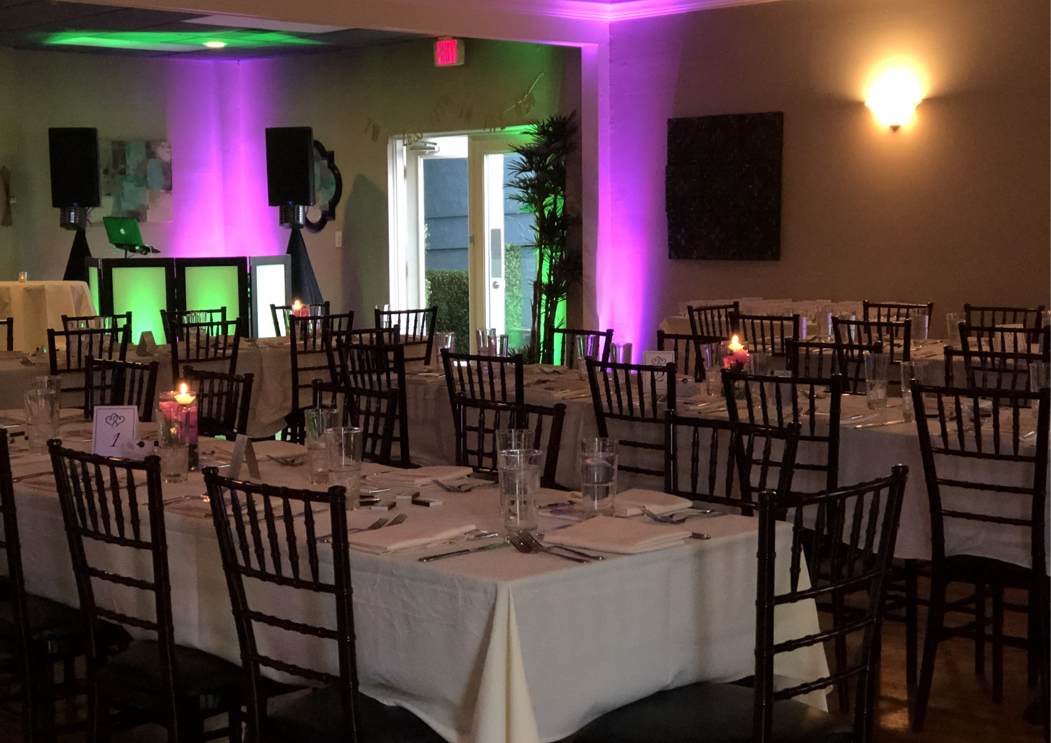 Small event hall with tables decorated for an event.  Colorful uplighting.