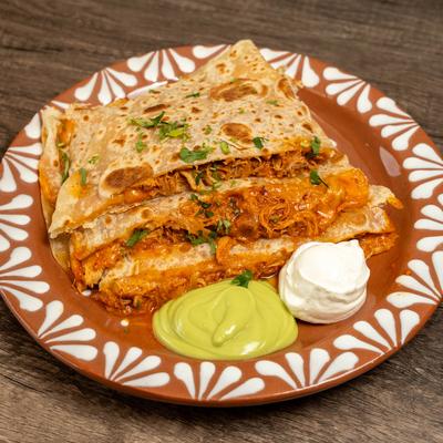 Chicken quesadilla served with sour cream and avocado sauce on a patterned plate.
