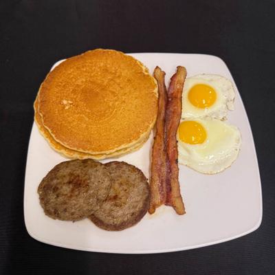 Breakfast plate with pancake, bacon, sausage patties, hash brown and fries eggs.