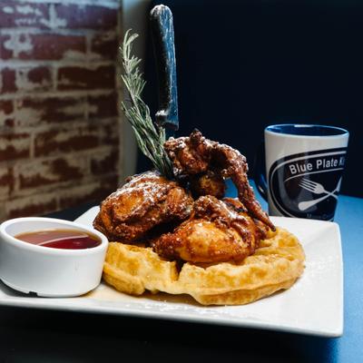 Chicken and waffles with powdered sugar, rosemary garnish, and syrup on the side.