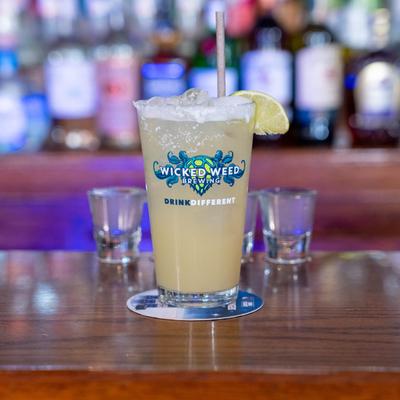 Margarita in a pint glass flanked by two shot glasses on the counter.