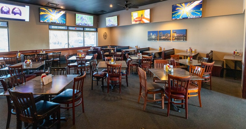 Interior of a dining restaurant with wooden tables, chairs, and multiple TVs