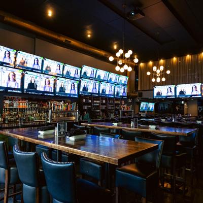 Interior, a bar with lots of wall mounted screens, seating area near the bar.