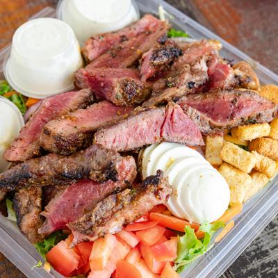 Grilled steak salad in a plastic takeaway container.
