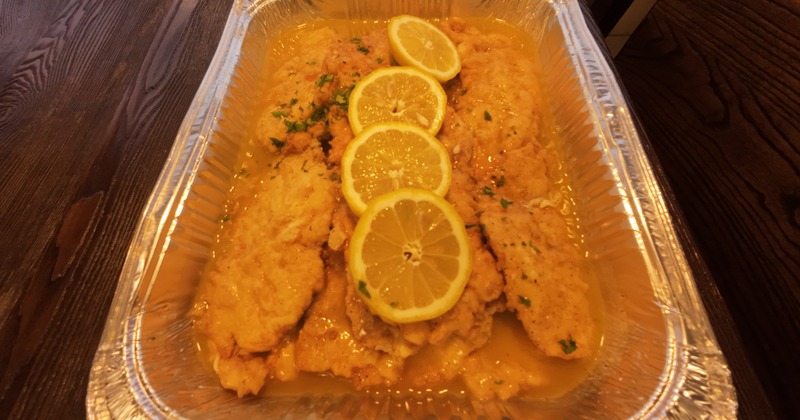 Fried fish fillets with sauce and lemon slices served in a foil tray