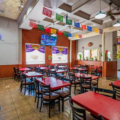 Mexican restaurant interior featuring red tables, tiled floors, and papel picado decorations.