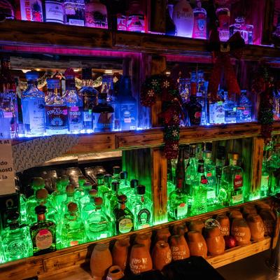 Bar, colorful bottles lit by blue and green lights, adorned with holiday bows and garlands.