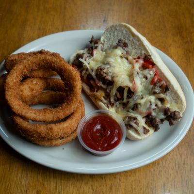 Philly cheesesteak sandwich with onions rings and ketchup.