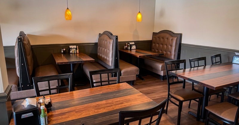 Cozy interior dining area with dining tables, chairs, and upholstered booths along the wall