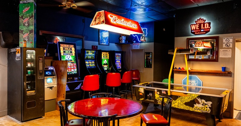 Sports bar interior, round table for four guests near arcade slot machines and air hockey table