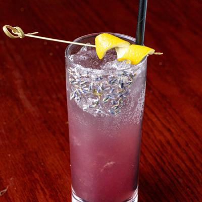 Mocktail with a purple hue, served in a highball glass, garnished with a lemon twist.