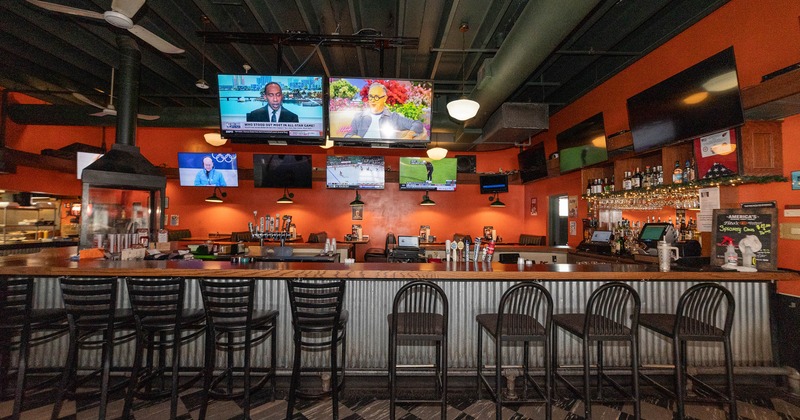 A long bar counter, high chairs , TVs and black-white floor.