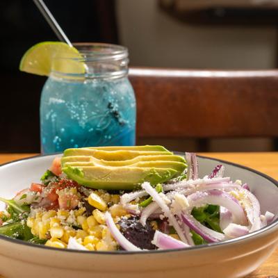 Salad served in a white bowl, accompanied by a blue beverage in a mason jar.