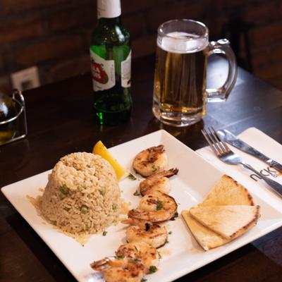 Plate with shrimp, rice and pita, accompanied with a glass of beer.
