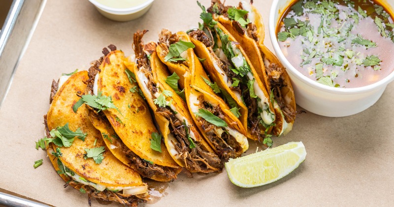 Crispy birria tacos served with broth and lime