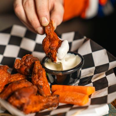 Person dipping chicken wing into white sauce.