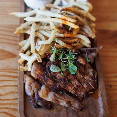 Grilled steak served sliced on a wooden board with a side of fries.