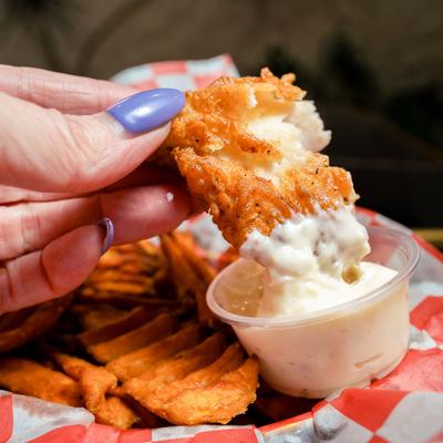 Hand dipping a piece of fried haddock into a cup of sauce.