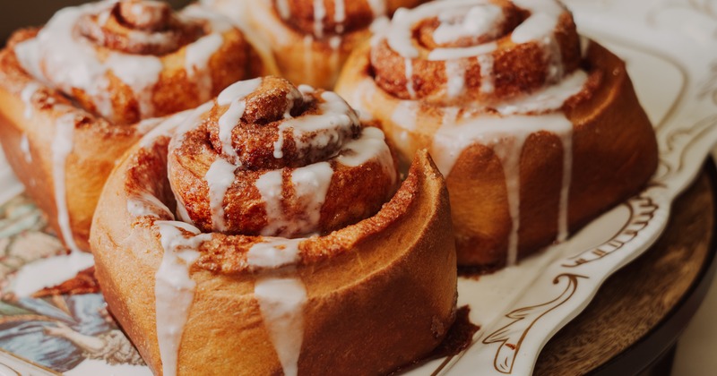 Close-up of four freshly baked cinnamon rolls on an ornate plate, drizzled with icing
