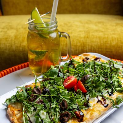 Flatbread with a generous amount of arugula and fresh tomatoes, alongside a drink.