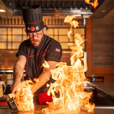 Hibachi chef creating a burst of fire on a hot iron griddle table.