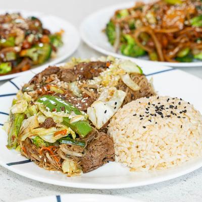 A plate of beef stir-fry served with rice, displayed on a table with other stir fry plates.