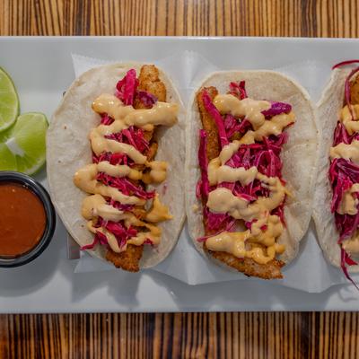 Crispy fish tacos with red cabbage slaw, creamy sauce, lime wedges, and dipping sauce.