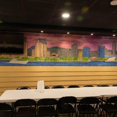A  mural of a vibrant cityscape adorns a wall in a room with a long table and chairs.